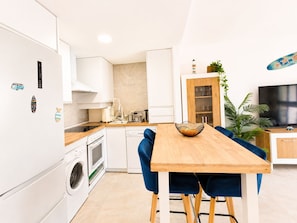 A modern kitchen with white cabinets, a wooden countertop, and a dining area with a wooden table and blue chairs. - El Mirador del Sol . (Conil de la Frontera)