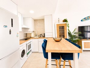 A modern kitchen with white cabinets, a wooden countertop, and a dining area with a wooden table and blue chairs. - El Mirador del Sol . (Conil de la Frontera)