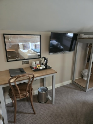 Ein Hotelzimmer mit Bett, Schreibtisch mit Stuhl, Fernseher, Spiegel und Mülleimer.