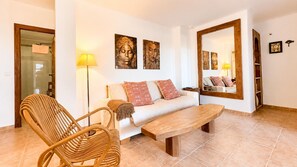 A living room with a sofa, a wooden coffee table, a wicker chair, and a floor lamp. - Casa Vega Vera Playa | Primera Línea de Playa | Beachtfront luxury Apartment with garden (Vera Playa)
