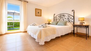 A bedroom with a bed, bedside lamps, a framed picture, and a view of greenery through a window. - Casa Vega Vera Playa | Primera Línea de Playa | Beachtfront Apartment with garden & 4 pools (Vera Playa)