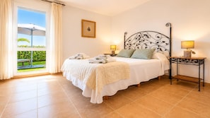 A bedroom with a bed, bedside lamps, a framed picture, and a view of greenery through a window. - Vera Playa Beachtfront Apartment with garden & 4 Pools (Vera Playa)