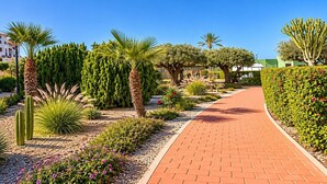 A paved pathway lined with various plants and cacti, leading to a building with a green roof. - Casa Vega Vera Playa | Primera Línea de Playa | Beachtfront Apartment with garden & 4 pools (Vera Playa)
