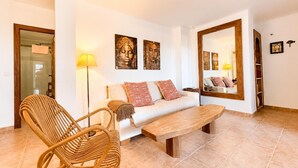 A living room with a sofa, a wooden coffee table, a wicker chair, and a floor lamp. - Casa Vega Vera Playa | Primera Línea de Playa | Beachtfront Apartment with garden & 4 pools (Vera Playa)