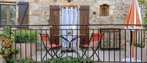 A stone building with a balcony, a table with chairs, and a small window.