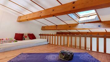 A room with a sloped ceiling, wooden beams, a window, a sofa with cushions, and a yoga mat.