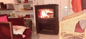 A cozy living room with a wood-burning stove, a wicker chair, and a red sofa.
