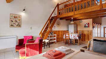 Een ruime woonkamer met een houten trap, een eettafel en een rode fluweelstoel.
