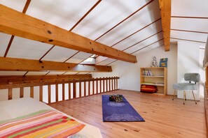 Ein Zimmer mit schrägem Dach, Holzbalken, einer Holzbank, einer Yogamatte, einem Bücherregal und einem Stuhl.