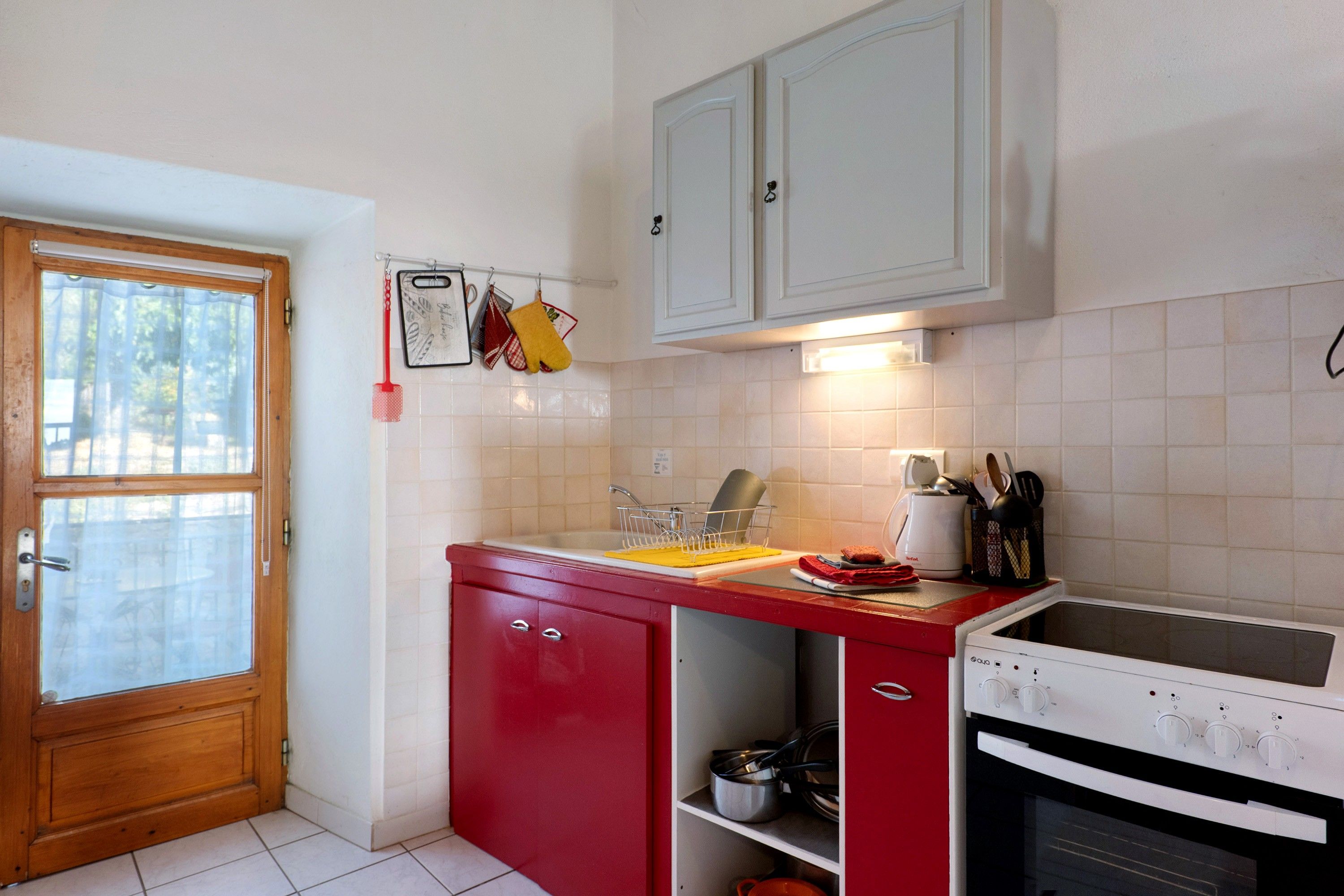 Eine Küche mit roter Arbeitsplatte, weißen Schränken, einem weißen Backofen und einer Tür mit Fenster.