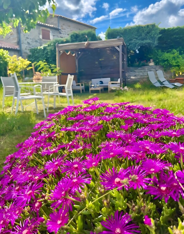 A garden with a patio area featuring outdoor furniture and a view of a building in the background.