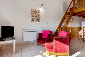 Een woonkamer met een flatscreen televisie, een witte airconditioner, een rode fluweelbank en een houten trap.