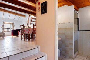 A room with a wooden ceiling, a dining area with a table and chairs, and a bathroom with a shower.