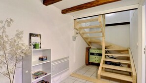 A room with a wooden staircase, a white shelving unit with books, and a green chest of drawers.