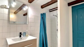 A bathroom with white tiles, a mirror, a sink with a faucet, a shower with a blue curtain, and a blue door.