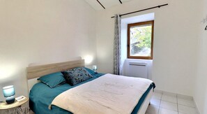 A bedroom with a bed, a nightstand, a lamp, a window with curtains, and a radiator.