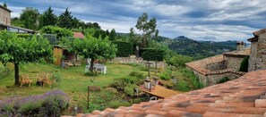 Un bâtiment rustique en pierre, doté d’un jardin, d’un espace extérieur aménagé pour s’asseoir et offrant une vue sur les collines environnantes.