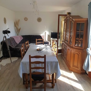 Uma sala de jantar com uma mesa posta para quatro pessoas, uma televisão, um armário e uma câmara sobre um tripé.