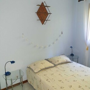 Um quarto com uma cama, uma mesinha, um abajur e um objeto decorativo na parede.
