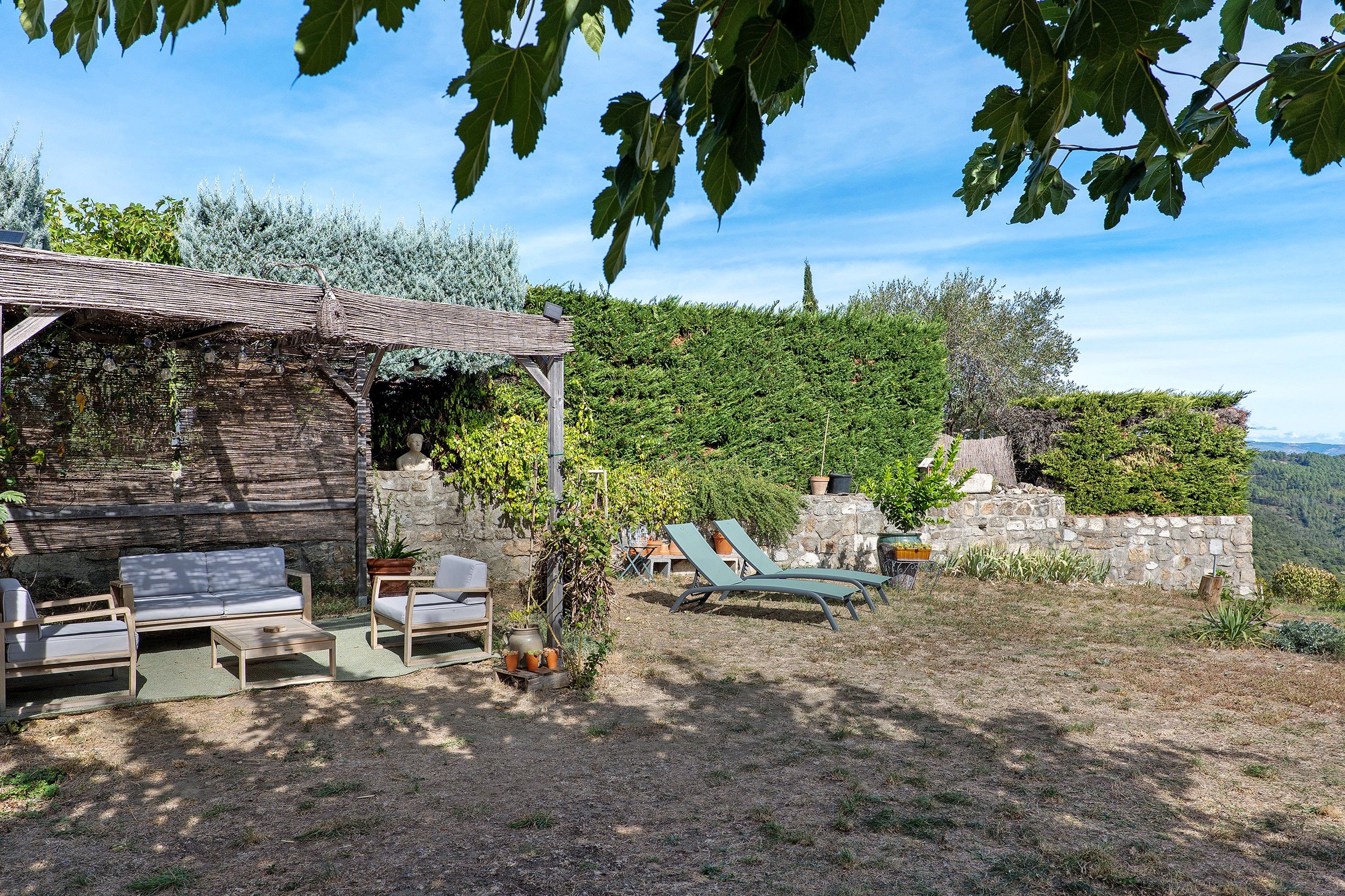 Un espace extérieur aménagé dans un style rustique, avec un mur en pierre et une pergola.