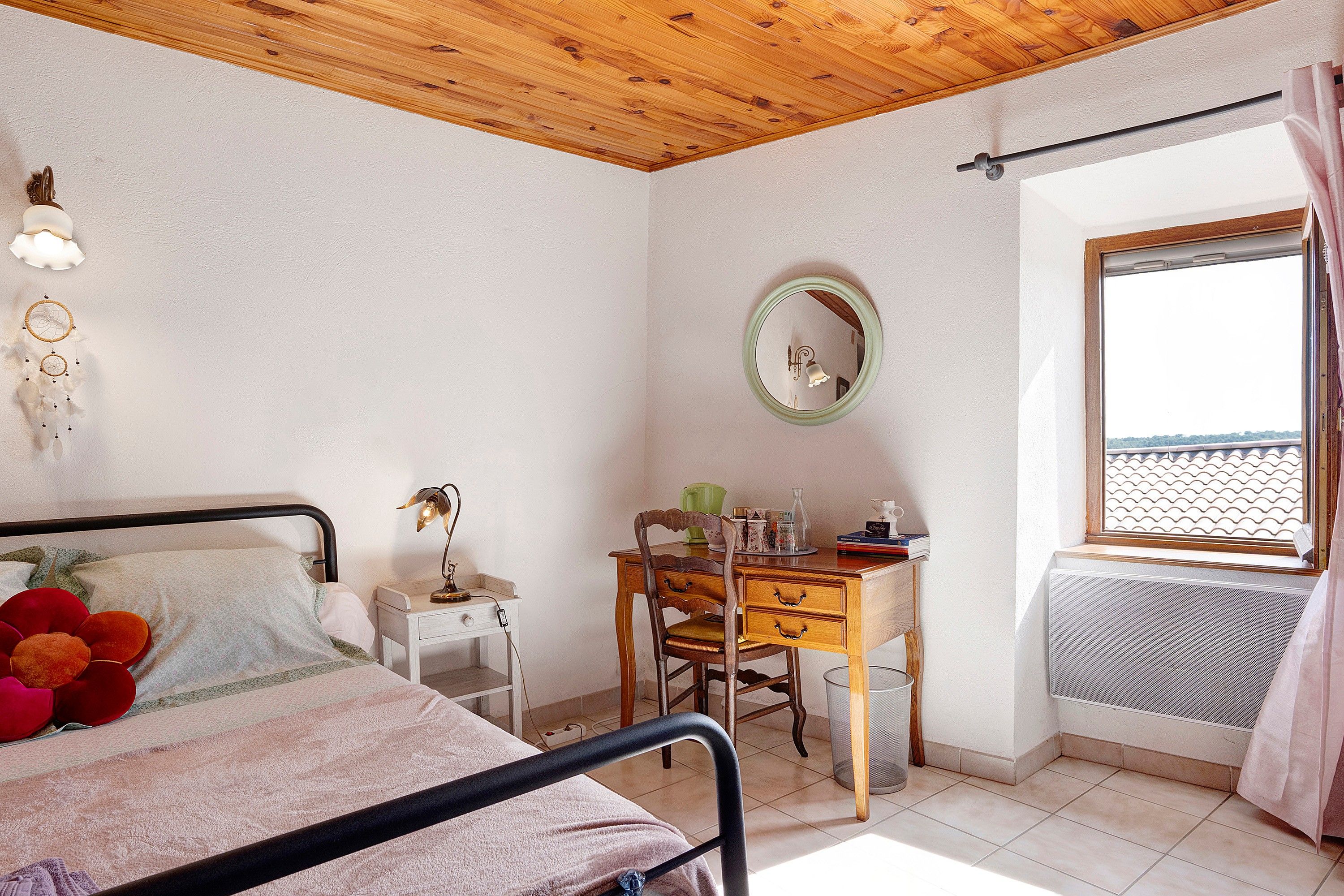 A bedroom with a bed, a desk, a chair, a window, and a mirror.
