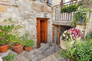 A stone building with a wooden door, potted plants, and a flower bed.