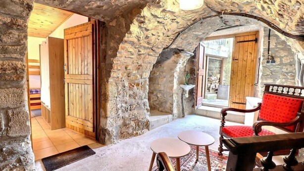 A stone-walled room with a wooden door, a red chair, and a small table.
