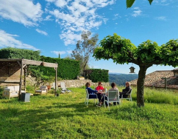 A group of people seated at a table outdoors, with a pergola and stone walls in the background. - Guest Room “L’Adrienne” with Shared Garden and Wi-Fi (Chazeaux)