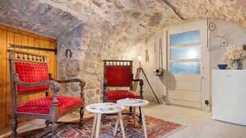 A room with a stone wall, a wooden door, a red upholstered chair, a small table with papers, and a white refrigerator.