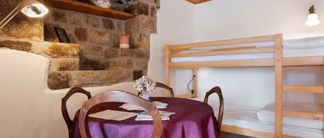 A room with a bunk bed, a stone wall, a table with a purple tablecloth, and a chair.