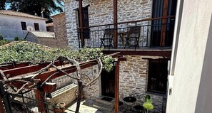 A stone building with a balcony, a small outdoor seating area, and a gate with vines.