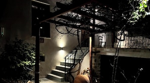 Una escalera con barandilla de metal, una luz adosada a la pared y una puerta con la etiqueta '1-4' en un espacio interior tenuemente iluminado.