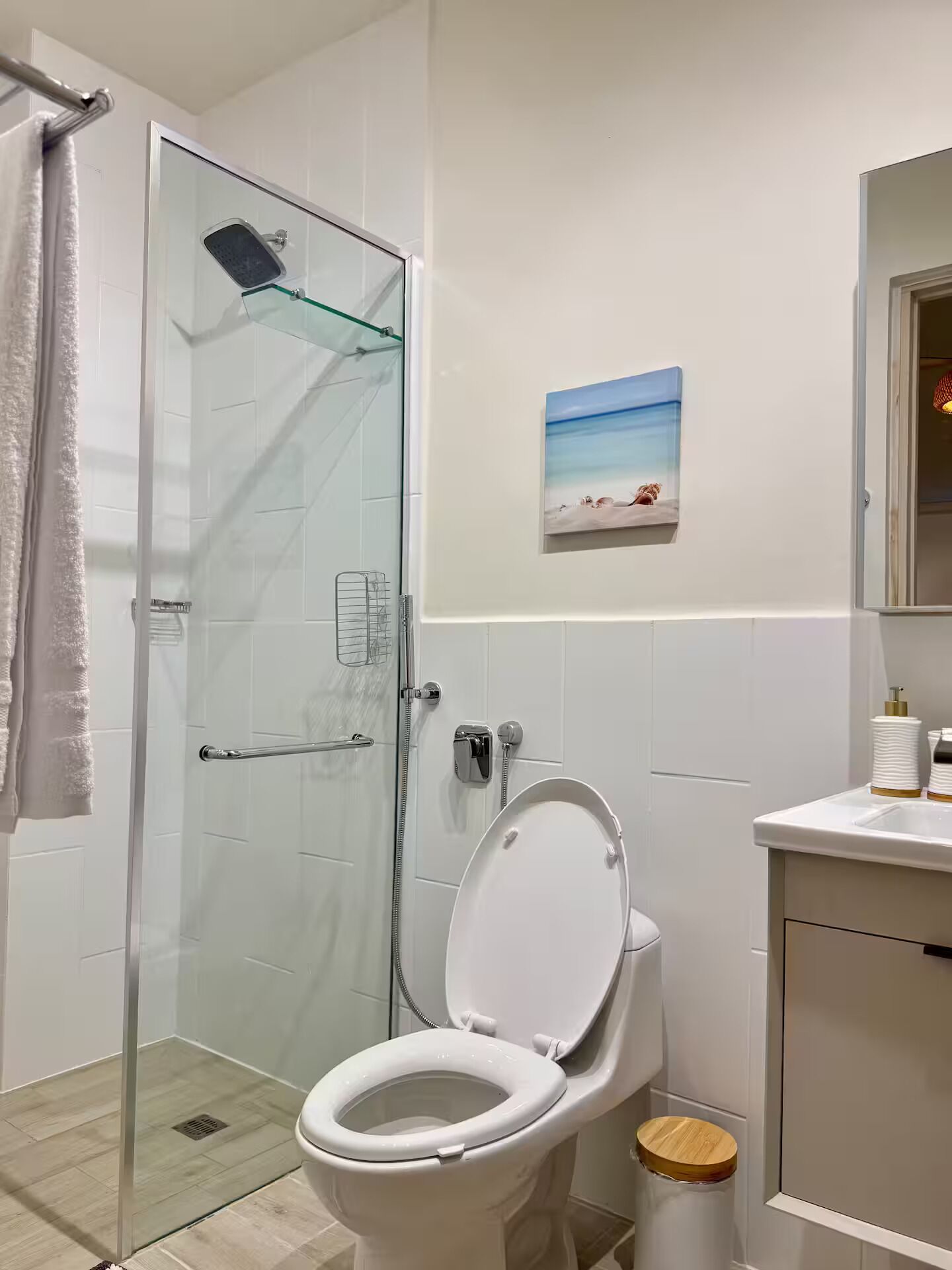 Un baño con cabina de ducha de vidrio, inodoro, lavamanos con espejo y una pequeña imagen colgada en la pared.