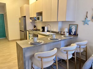 A modern kitchen with a central island, bar stools, a microwave, and a coffee maker. - Apartamento con increíble vista frente al mar (punta chame)