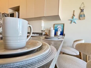 Cucina con mobili bianchi, microonde, macchina da caffè e zona pranzo con decorazione a stella marina.