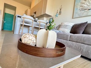 Un soggiorno moderno con un divano grigio, un tavolino da caffè con oggetti decorativi, un'area cucina sullo sfondo e una porta color petrolio.