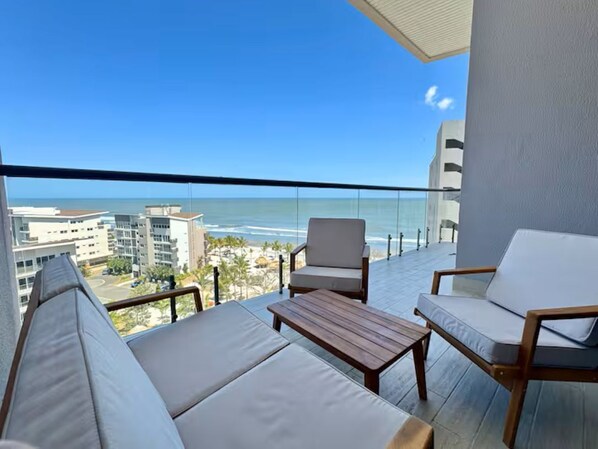 Un balcone con vista sull'oceano, un divano, una sedia e un tavolino.