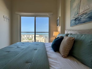 Ein Schlafzimmer mit großem Fenster, einem Bett, einem Gemälde und Blick auf Gebäude und Wasser.