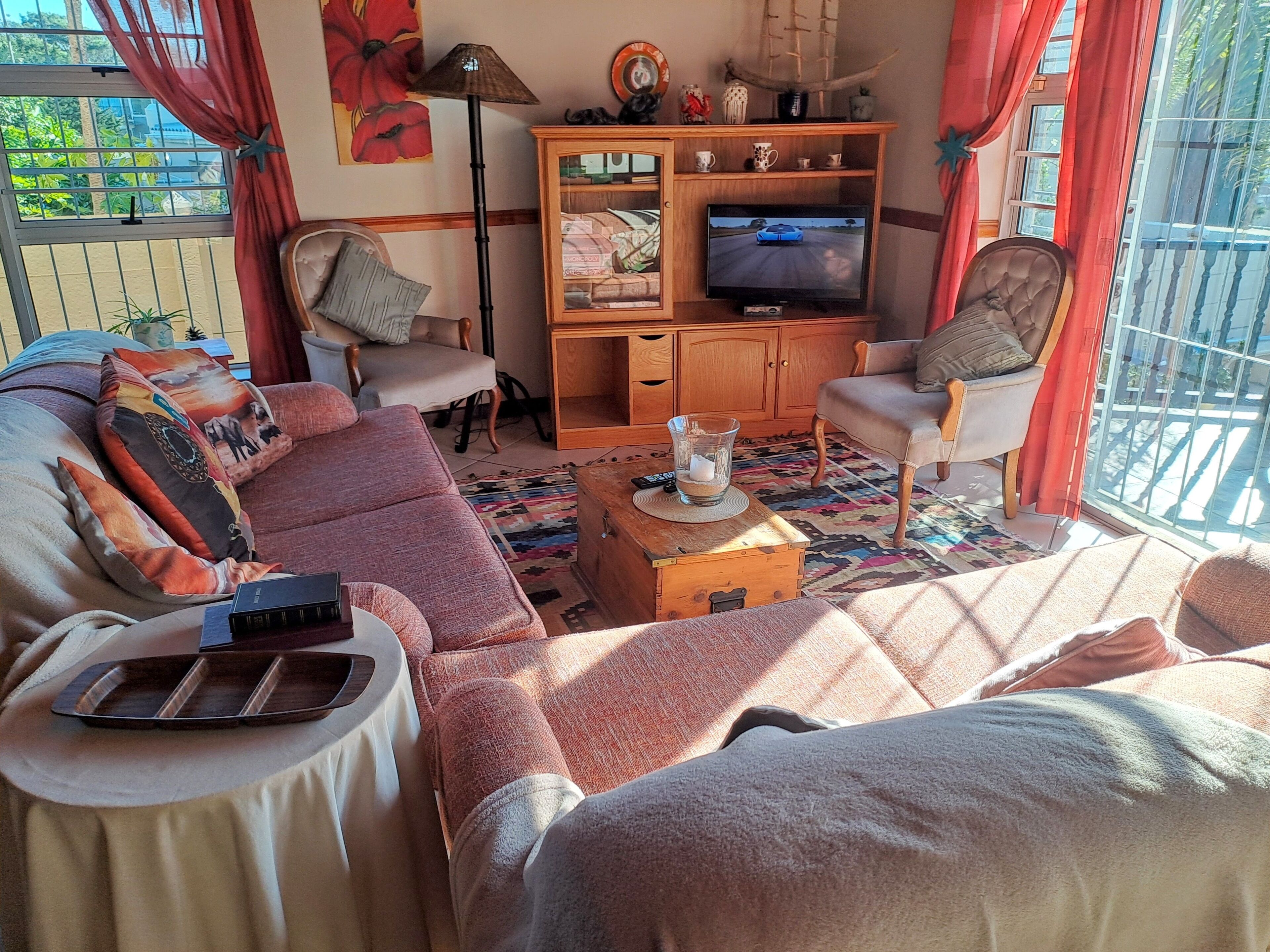Uma sala de estar aconchegante com sofá, poltronas, televisão e um aparador de madeira.