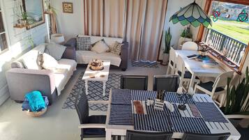 Un salón acogedor con sofá, mesa de comedor, sillas y un balcón con plantas.