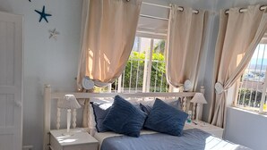 A bedroom with a bed, nightstands, a window with curtains, starfish wall decor, and a ceiling fan. - BayView Guest House  (Jeffreys Bay)