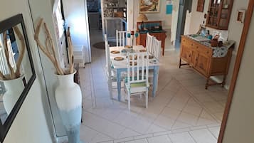 Un comedor con una mesa dispuesta para dos personas, una cocina al fondo y un jarrón grande con ramas.