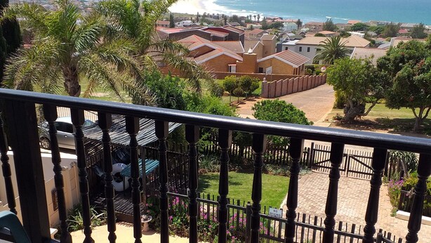 A balcony with a view of a beach and ocean, a swimming pool, and a fenced garden area. - BayView Guest House  (Jeffreys Bay)