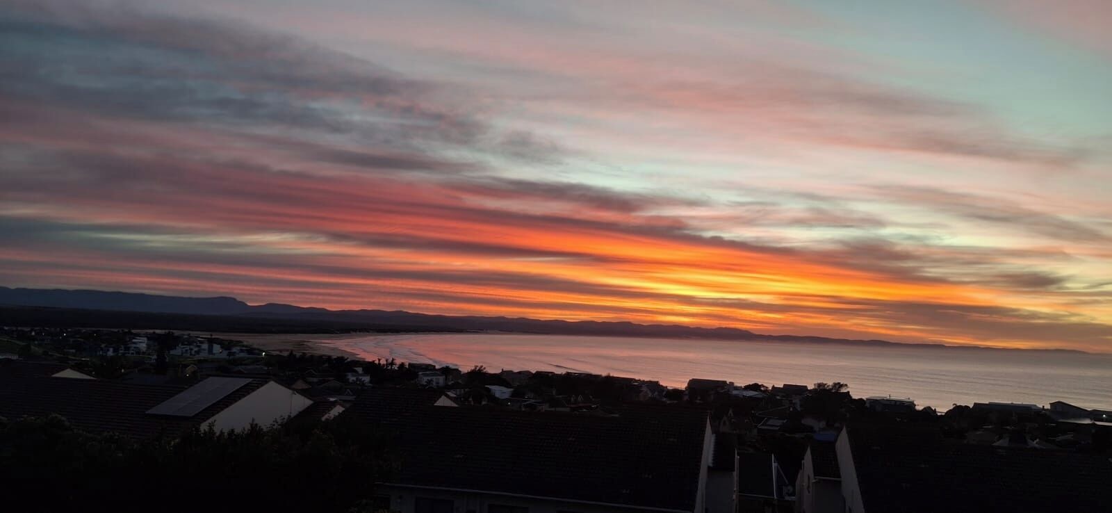 A sunset over a coastal town with visible buildings and a clear sky.
