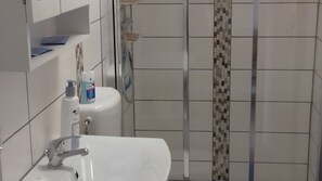 Ein Badezimmer mit weißem Waschbecken, einem Spiegel, einer Duschkabine mit Glastür und einer gefliesten Wand.