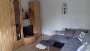 Ein modernes Wohnzimmer mit einem grauen Sofa, einem kleinen Tisch und einem Fernseher auf einer Holzkommode.