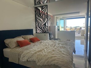 Ein Schlafzimmer mit Bett, Kissen, einer Wanddekoration und Blick ins Freie.