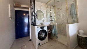 A modern bathroom with a washing machine, a sink, and a glass shower enclosure. - Naturist Village - Heliopolis AB - 30 m² - ocean view (Agde)