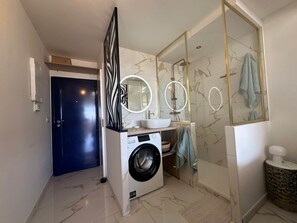 Ein modernes Badezimmer mit Waschmaschine, Waschbecken und einer Duschkabine aus Glas.