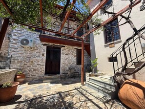 A stone building with a wooden door and a small outdoor seating area. - Tsagarakis Guesthouse & Pool Room .5 with Courtyard View, Wi-Fi and Air Conditioning (Xinovrysi)